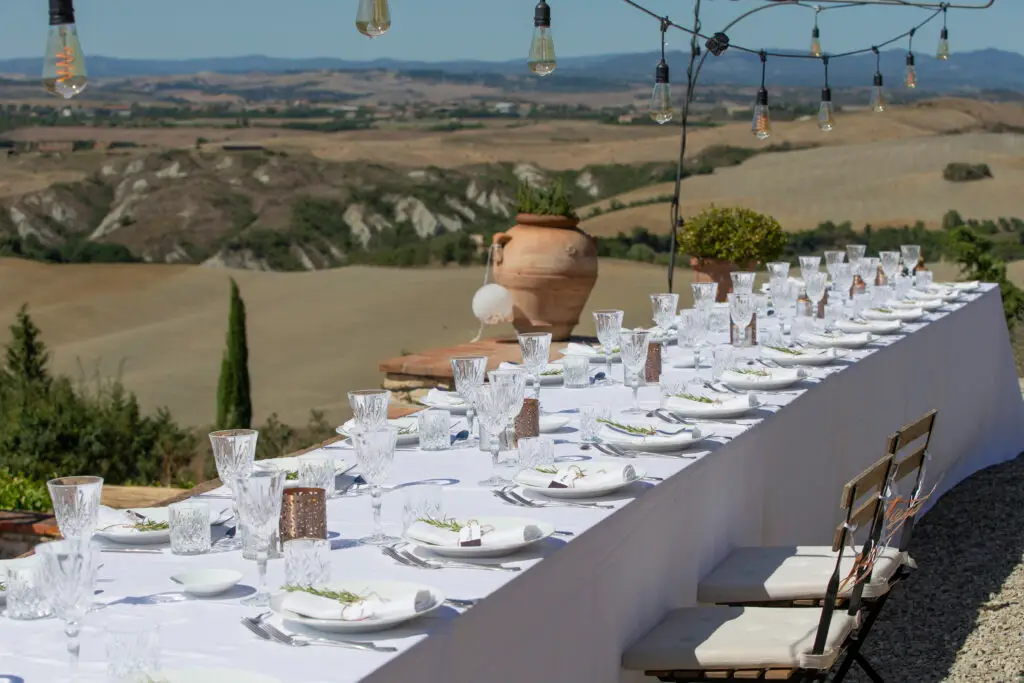 Lange, festlich gedeckte Tafel im Freien mit Blick auf eine hügelige Landschaft.
